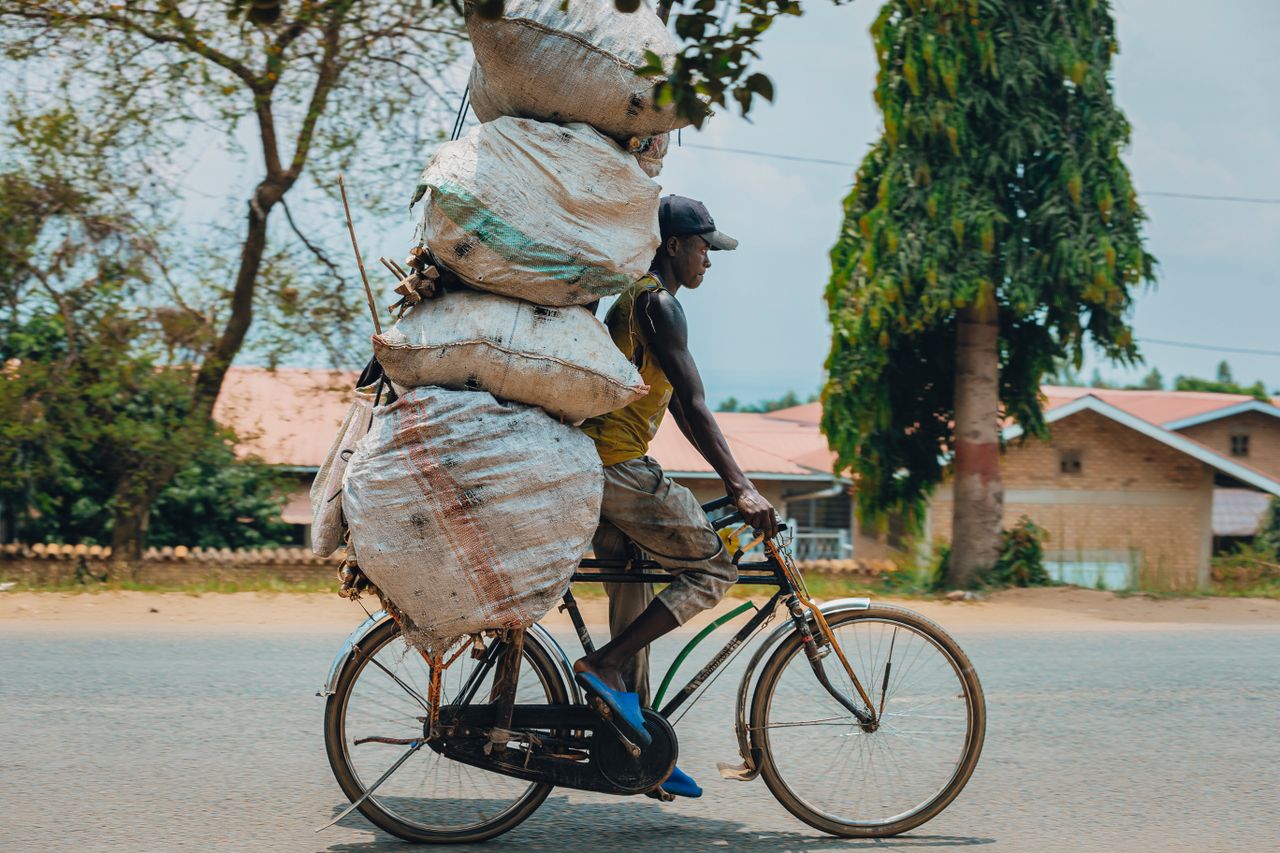 A man skillfully rides a bicycle carrying multiple large bags on an urban street.